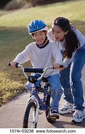 Stock Photo - Mother helping her son ride a bicycle. Fotosearch