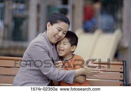 Mother hugging her son sitting on a park bench View Large Photo Image Stock Image - Mother hugging her son sitting on a park bench. Fotosearch