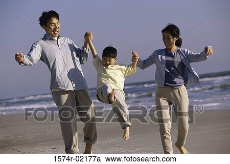 Stock Image - Parents carrying their son on the beach. Fotosearch