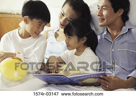 Stock Photo - Parents lying on a bed with their son and daughter. Fotosearch