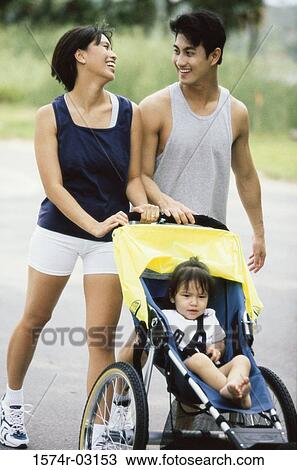Stock Image - Parents walking with their baby girl in a stroller. Fotosearch