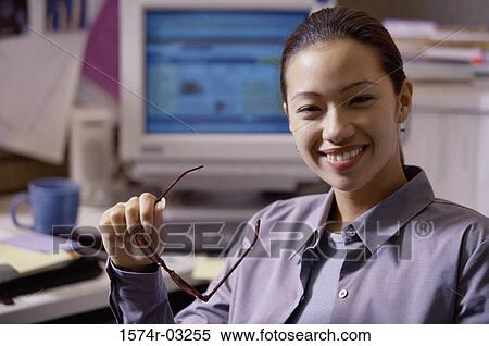 Stock Photography - Portrait of a businesswoman holding her eyeglasses in an office. Fotosearch