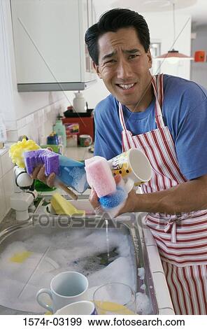 Stock Photo - Portrait of a young man washing dishes in the kitchen. Fotosearch