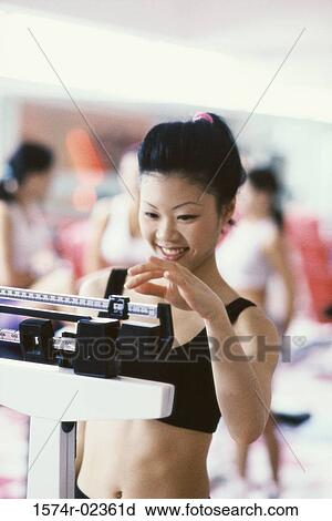 Stock Image - Young woman standing on a weight scale. Fotosearch