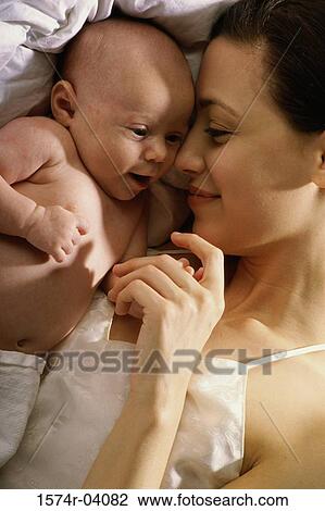 Stock Image - Mother and her baby boy lying on a bed. Fotosearch