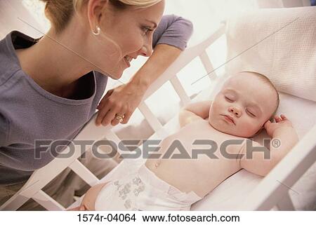 Picture - Mother looking at her baby boy in a crib. Fotosearch