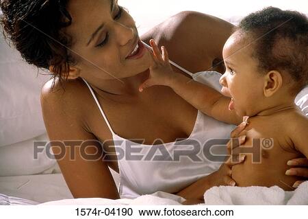 Stock Image - Mother lying on a bed with her baby girl. Fotosearch