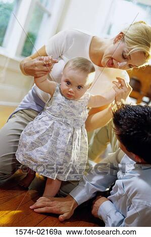 Stock Image - Parents helping their baby girl learn how to walk. Fotosearch
