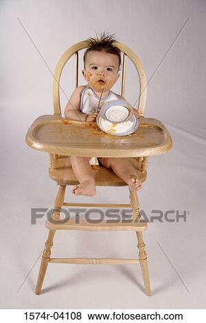 Stock Photo - Portrait of a baby boy sitting in a high chair playing with a bowl. Fotosearch