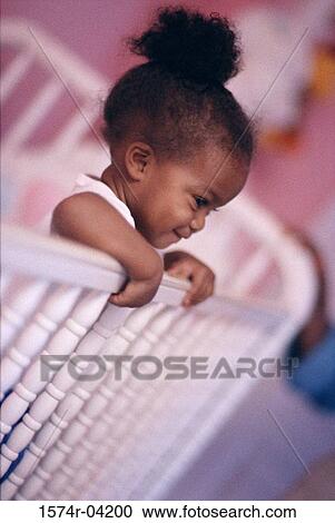 Stock Image - Side profile of a baby girl standing in a crib. Fotosearch