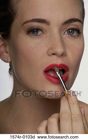 Stock Image - Close-up of a young woman applying lipstick with a brush. Fotosearch