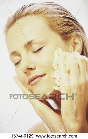 Close-up of a young woman cleaning her face with a sponge View Large Photo Image Stock Photo - Close-up of a young woman cleaning her face with a sponge. Fotosearch