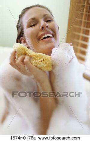 Stock Image - Close-up of a young woman holding a sponge in a bubble bath. Fotosearch
