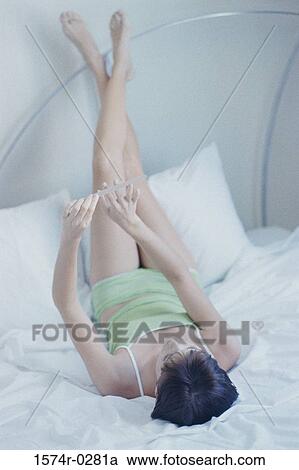 High angle view of a young woman lying on a bed filing her nails View Large Photo Image Stock Image - High angle view of a young woman lying on a bed filing her nails. Fotosearch