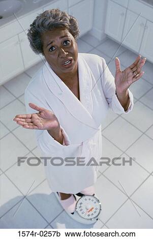 Stock Image - Portrait of a woman standing on a scale. Fotosearch