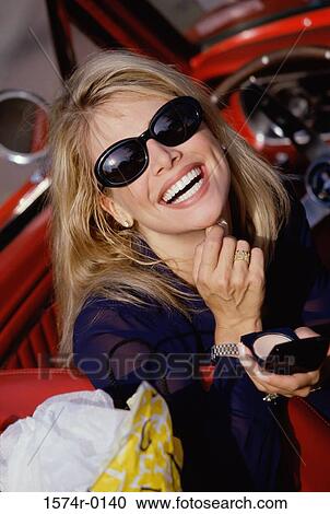 Stock Image - Portrait of a young woman sitting in a convertible applying powder from a compact. Fotosearch