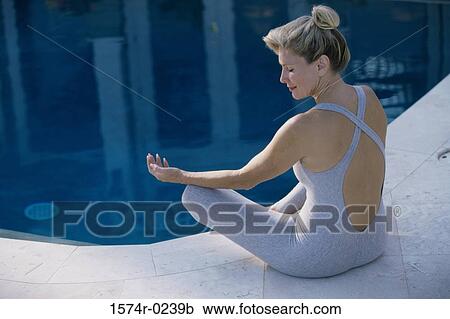 Stock Image - Rear view of a woman meditating beside a swimming pool. Fotosearch