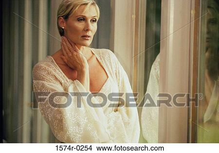 Woman wearing a robe standing with her hand on her neck View Large Photo Image Picture - Woman wearing a robe standing with her hand on her neck. Fotosearch