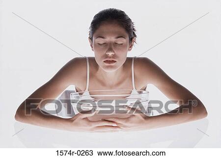 Stock Image - Young woman inhaling steam from a bowl of water. Fotosearch