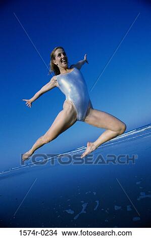 Picture - Young woman jumping at the beach. Fotosearch