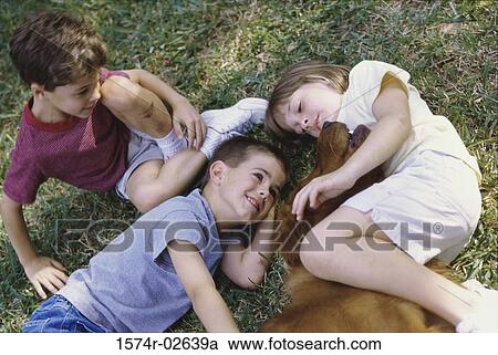 High angle view of two boys and a girl lying on grass with a dog View Large Photo Image Stock Image - High angle view of two boys and a girl lying on grass with a dog. Fotosearch