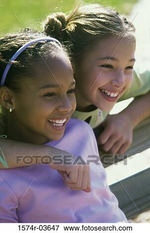 Two girls sitting on a bench smiling View Large Photo Image Stock Photo - Two girls sitting on a bench smiling. Fotosearch