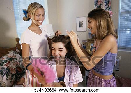 Picture - Two teenage girls styling their friend's hair. Fotosearch