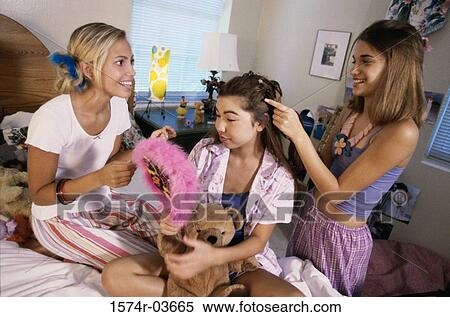 Stock Photography - Two teenage girls styling their friend's hair. Fotosearch