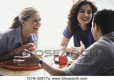 Stock Image - Two young women and a young man sitting in a restaurant. Fotosearch