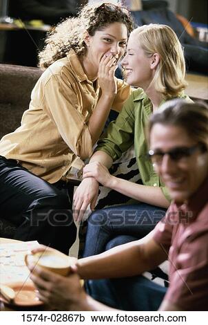 Stock Image - Two young women and a young man sitting in a cafeteria. Fotosearch
