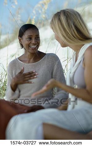 Two young women sitting together talking View Large Photo Image Stock Photo - Two young women sitting together talking. Fotosearch