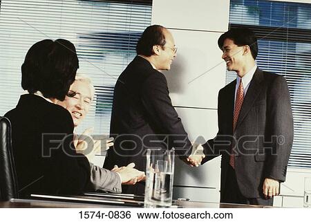 Stock Photograph - Business executives shaking hands in a meeting. Fotosearch