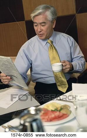 Businessman holding a cup and reading a newspaper View Large Photo Image Stock Photography - Businessman holding a cup and reading a newspaper. Fotosearch