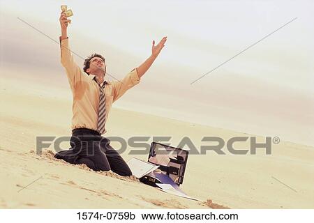 Stock Image - Businessman kneeling on the beach with his arms raised. Fotosearch