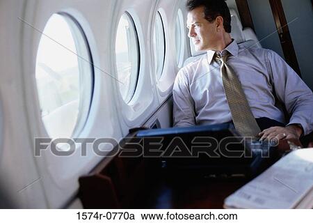 Stock Image - Businessman sitting in an airplane looking out the window. Fotosearch