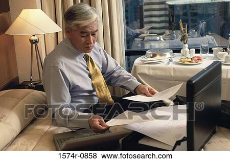 Stock Photo - Businessman sitting on the edge of a bed holding documents. Fotosearch