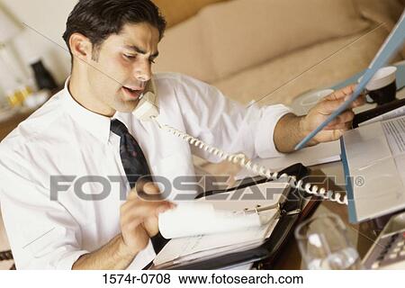 Businessman talking on a telephone and reading a diary View Large Photo Image Stock Photo - Businessman talking on a telephone and reading a diary. Fotosearch