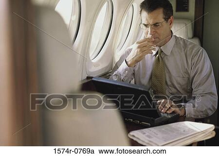 Businessman using a laptop in an airplane View Large Photo Image Stock Image - Businessman using a laptop in an airplane. Fotosearch