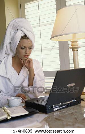 Stock Image - Businesswoman in a bathrobe seated in front of a laptop. Fotosearch