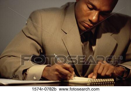 Stock Image - Close-up of a young businessman making notes on his desk. Fotosearch
