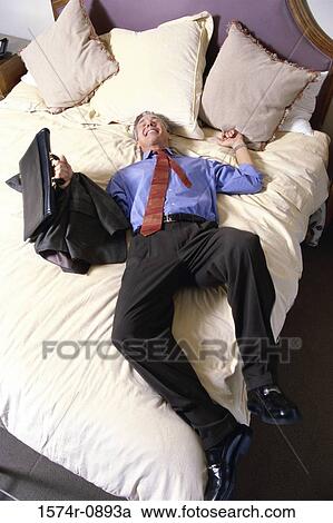 Stock Image - High angle view of a businessman lying on a bed in a hotel room. Fotosearch