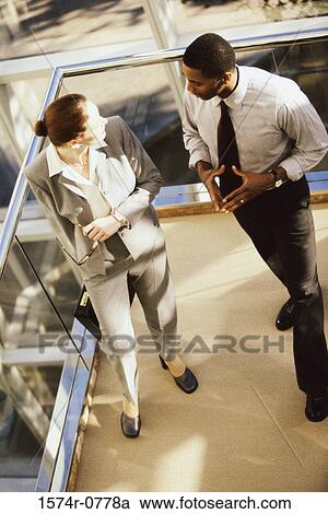 Stock Image - High angle view of a businesswoman and a businessman discussing in an office. Fotosearch
