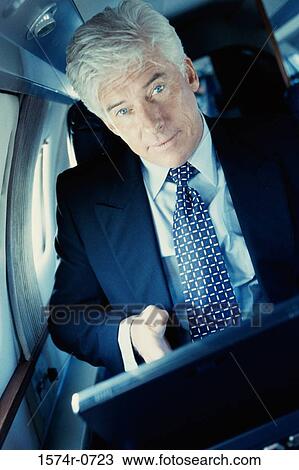 Portrait of a businessman holding a laptop sitting in an airplane View Large Photo Image Stock Image - Portrait of a businessman holding a laptop sitting in an airplane. Fotosearch