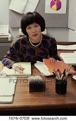 Portrait of a businesswoman seated behind a desk in an office View Large Photo Image Stock Image - Portrait of a businesswoman seated behind a desk in an office. Fotosearch