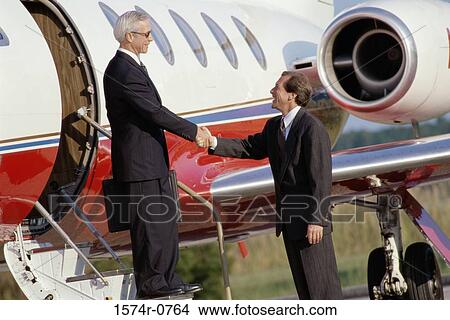 Picture - Two businessmen shaking hands near an airplane. Fotosearch