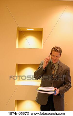 Stock Image - Businessman standing in a corridor using a mobile phone. Fotosearch