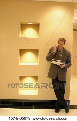 Businessman standing in a corridor using a mobile phone View Large Photo Image Stock Image - Businessman standing in a corridor using a mobile phone. Fotosearch