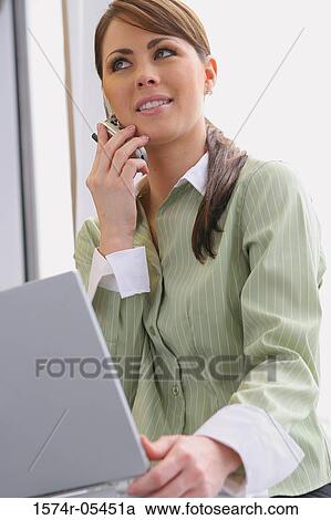 Close-up of a businesswoman holding a laptop using a mobile phone View Large Photo Image Stock Image - Close-up of a businesswoman holding a laptop using a mobile phone. Fotosearch