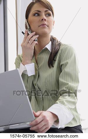 Close-up of a businesswoman holding a laptop using a mobile phone View Large Photo Image Stock Photography - Close-up of a businesswoman holding a laptop using a mobile phone. Fotosearch