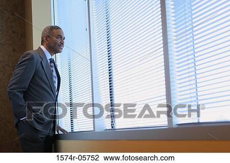 Stock Image - Side profile of a businessman looking through a window. Fotosearch